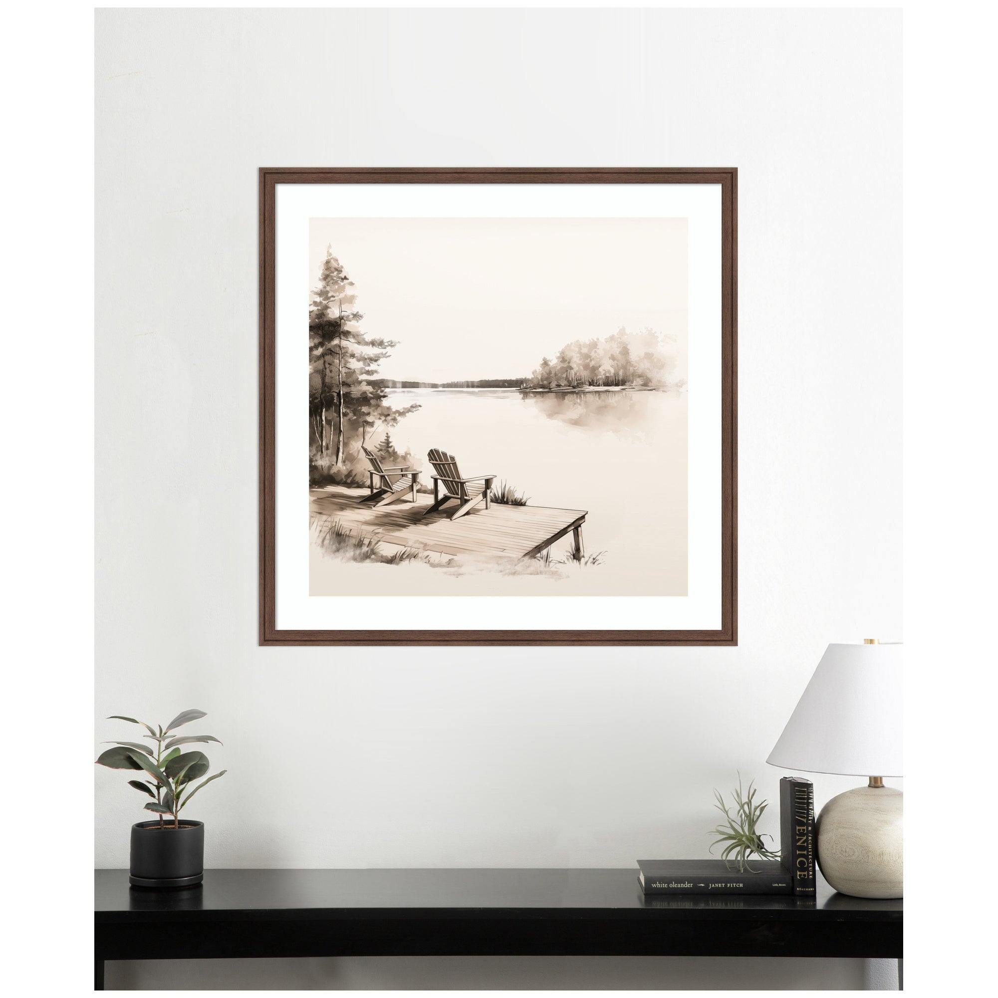 Framed artwork of a lakeside scene with Adirondack chairs on a white wall above a desk.