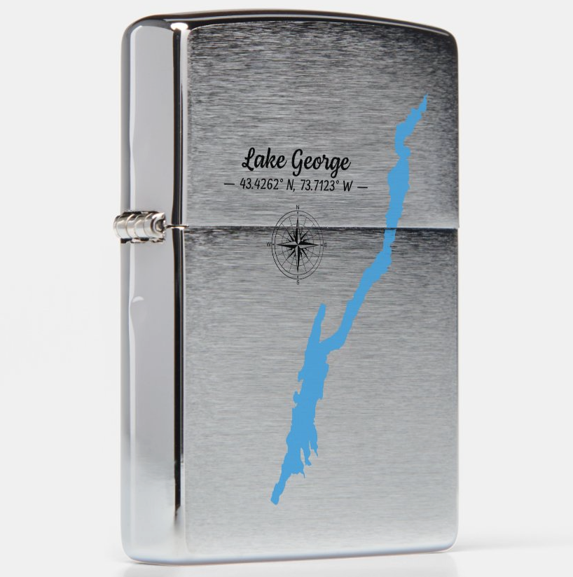 A silver metal lighter with a brushed finish, featuring a blue silhouette map of Lake George and engraved text with coordinates, shown on a light gray background.