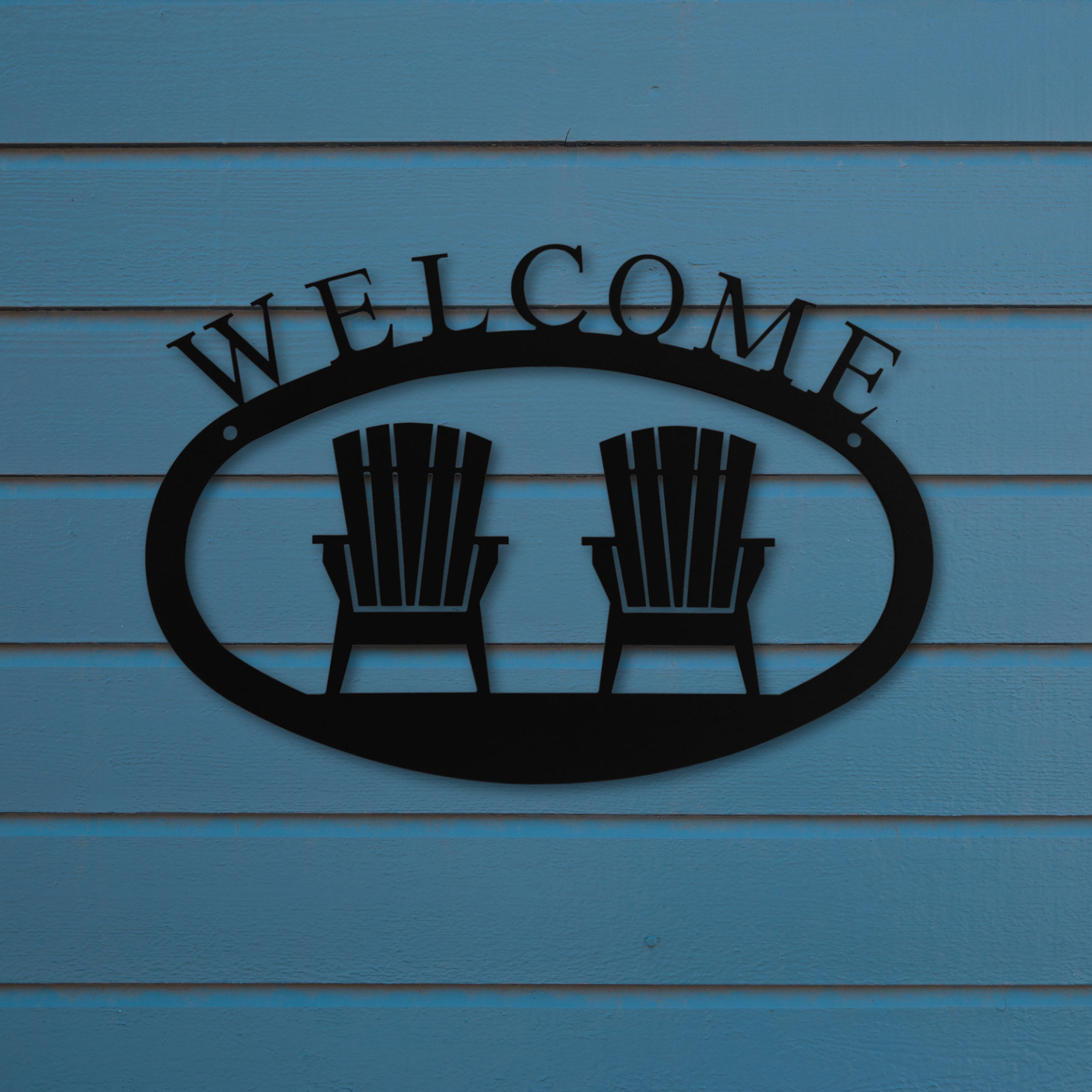 Metal 'Welcome' sign with two Adirondack chairs against a blue wooden background